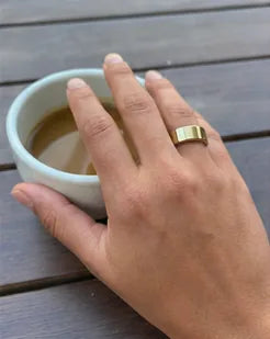 A hand wearing the gold Quriov Smart Ring, resting beside a coffee cup.