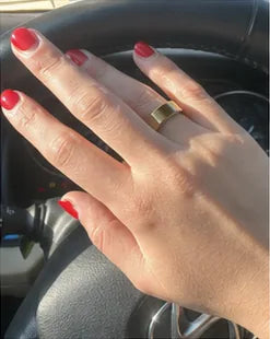 A hand with painted nails wearing the gold Quriov Smart Ring at the wheel.