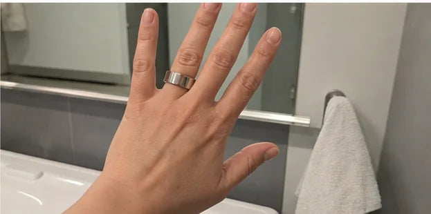 A hand wearing the silver Quriov Smart Ring in a bright bathroom.