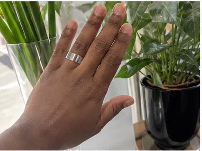A hand wearing the silver Quriov Smart Ring at home among houseplants.